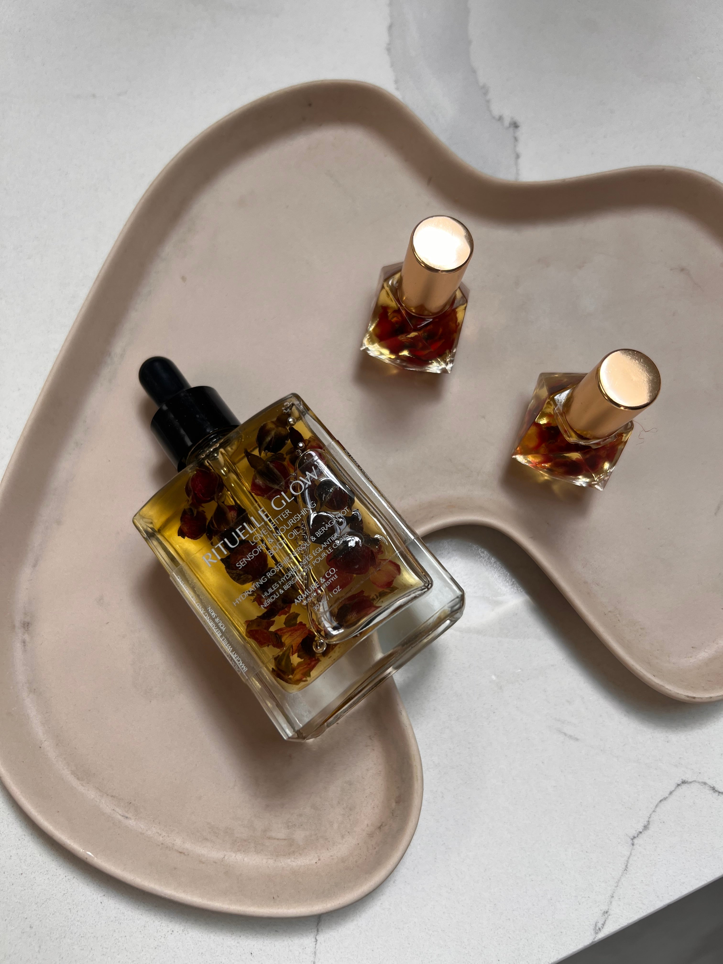 Two perfume oil bottles on a heart-shaped ceramic plate with a light background